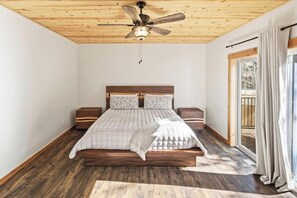 Une chambre avec un plafond en bois, un lit doté d’une tête de lit, deux tables de chevet et une vue sur l’extérieur grâce à une porte-fenêtre coulissante.