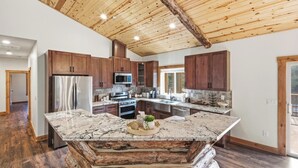 A spacious kitchen with wooden cabinets, a large island, and a rustic ceiling. - Custom Log Style Cabin! Foosball! BBQ! Decks! Fenced Yard! (Big Bear Lake)
