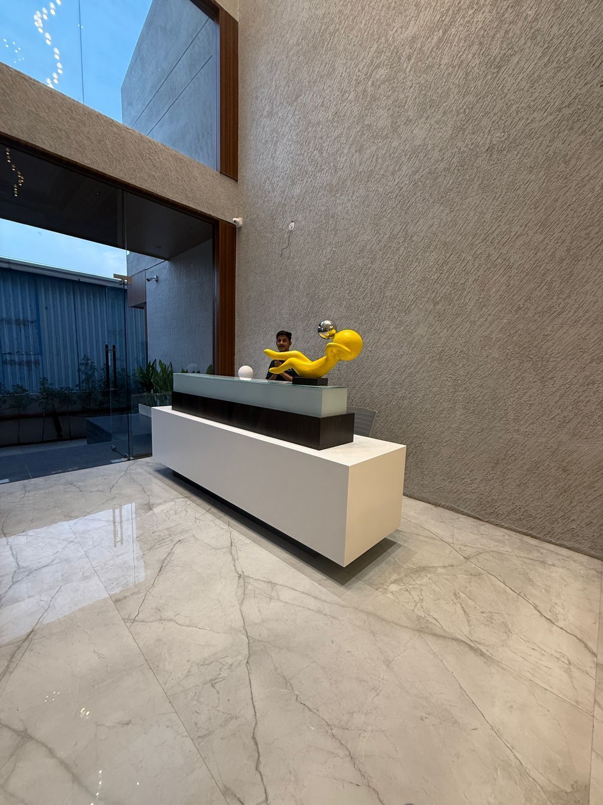 Una moderna recepción con diseño minimalista, suelo de mármol y un amplio ventanal con vistas a un edificio.