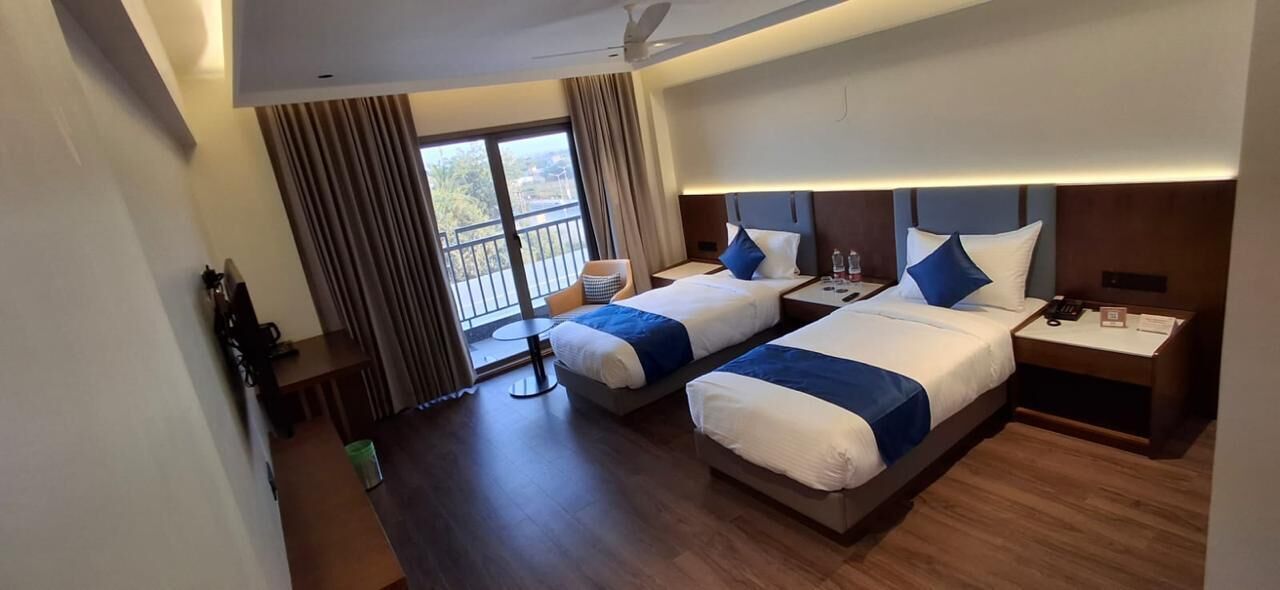 Habitación de hotel con dos camas, un balcón, un escritorio y una silla.