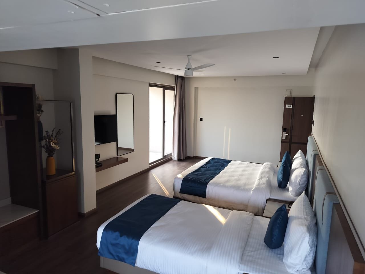 A hotel room with two beds, a flat-screen TV, a mirror, a wardrobe, and a plant.