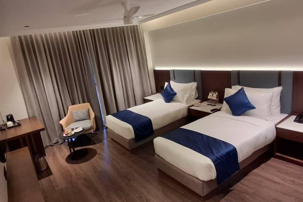 A hotel room with two beds, a desk, a chair, and a large window with curtains.
