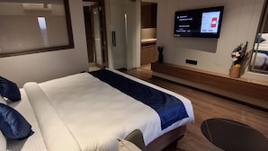 A modern hotel room with a large bed, a flat-screen TV mounted on the wall, a small desk, and a view of the city through the window. - Hotel StoneLeaf (Chhatrapati Sambhajinagar)