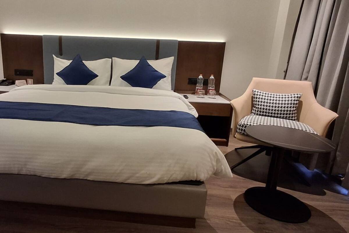 A modern hotel room with a large bed, a nightstand, a chair, and a desk.