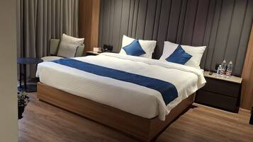 Una habitación de hotel moderna con una cama grande, una mesita de noche con lámpara y un pequeño mueble con botellas de agua.