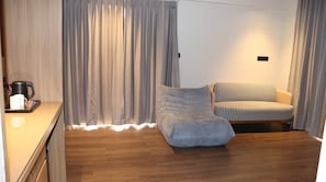 A room with a wooden floor, a sofa, a chair, and a coffee maker on a counter.