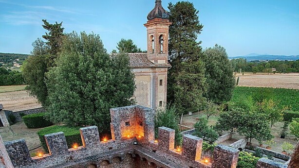 Un cortile con un lungo tavolo apparecchiato per mangiare, circondato da mura di pietra e una torre sullo sfondo.