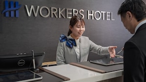 Un comptoir d’accueil d’hôtel avec une pancarte indiquant « HÔTEL POUR TRAVAILLEURS », un ordinateur portable, une tablette et un smartphone posés sur le comptoir.