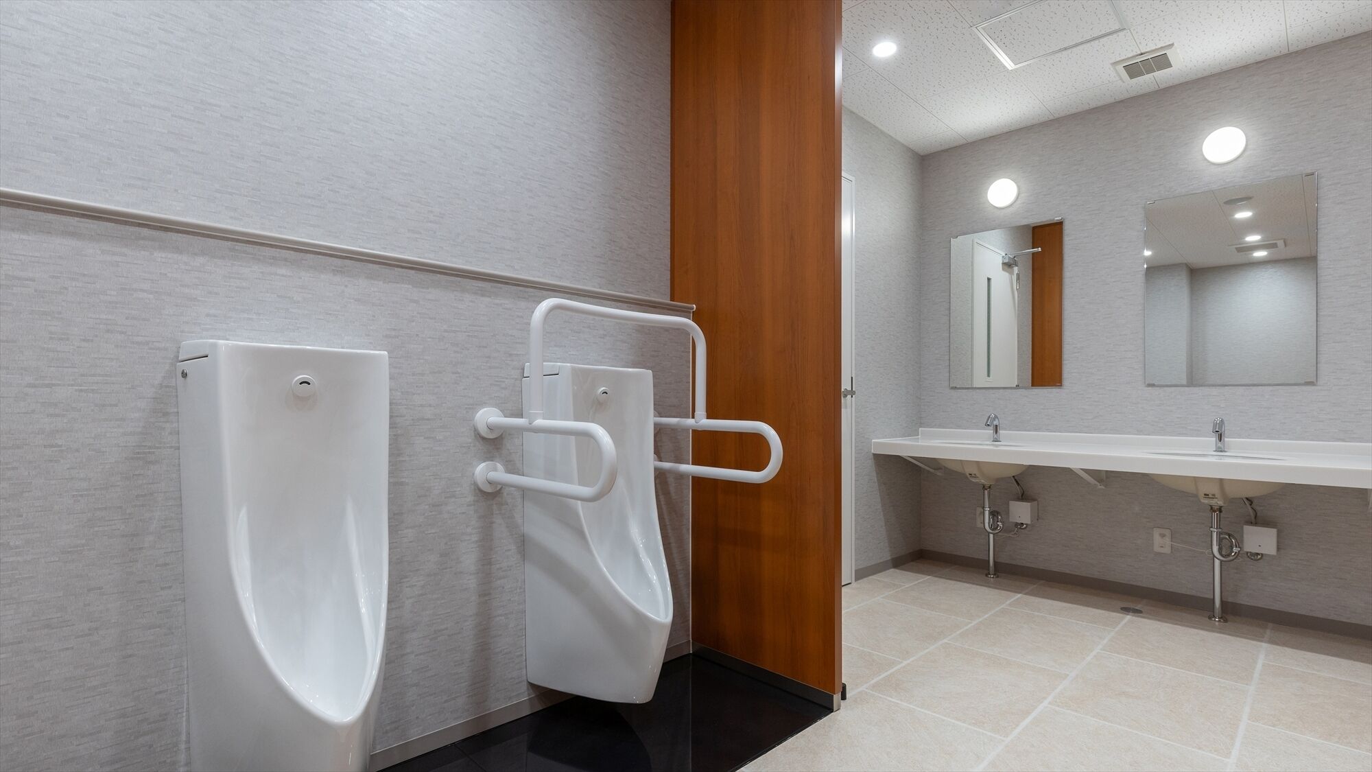 A modern bathroom with urinals, a handrail, a sink, and a mirror.