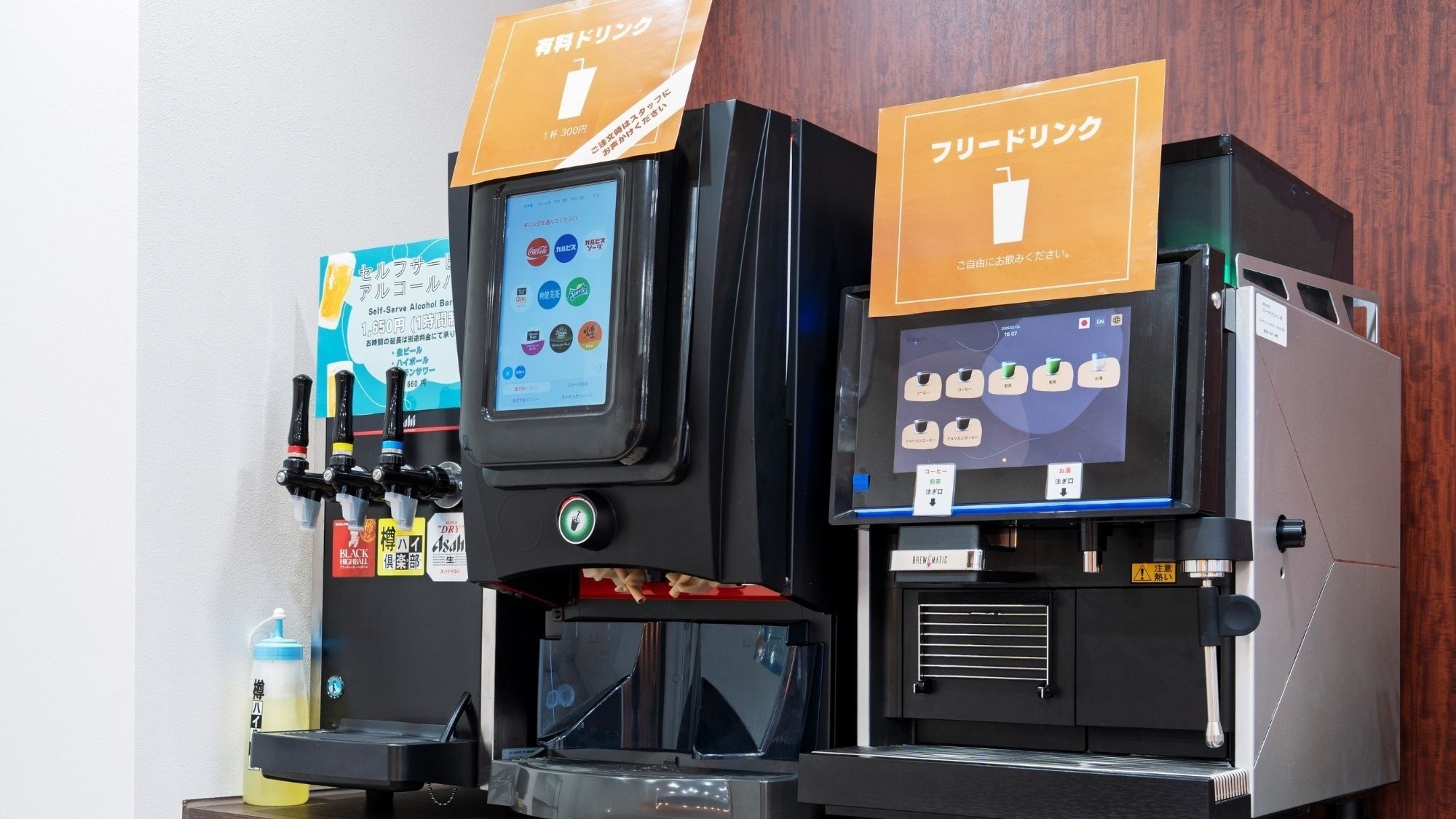 Two self-serve alcohol machines with digital interfaces, a bottle of water, and a menu board.