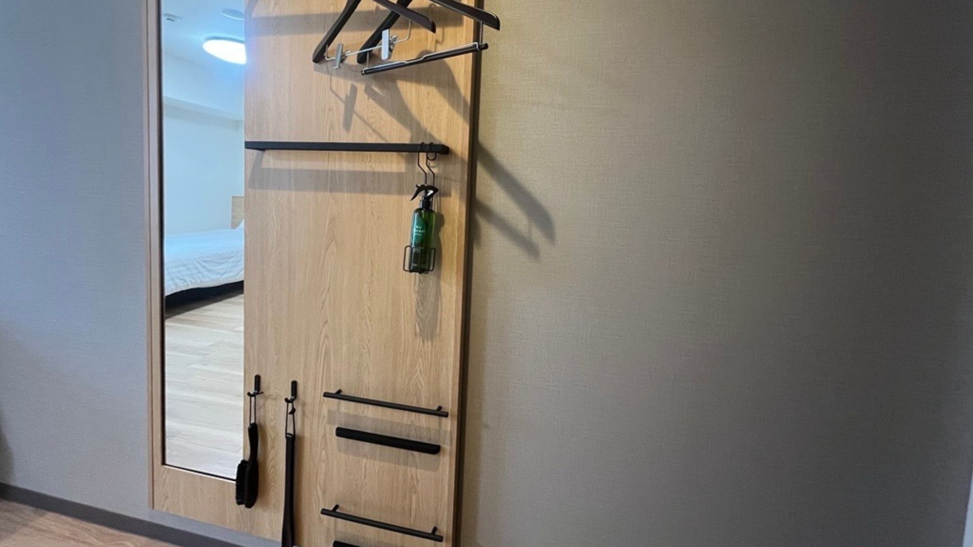 A wooden wardrobe with a mirror, a hanging rack, and a bottle of hand sanitizer.