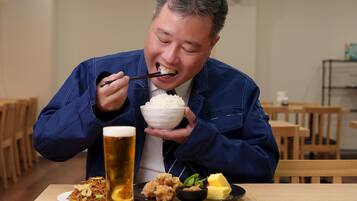 A person dining at a table with a bowl of rice, a glass of beer, and various dishes.