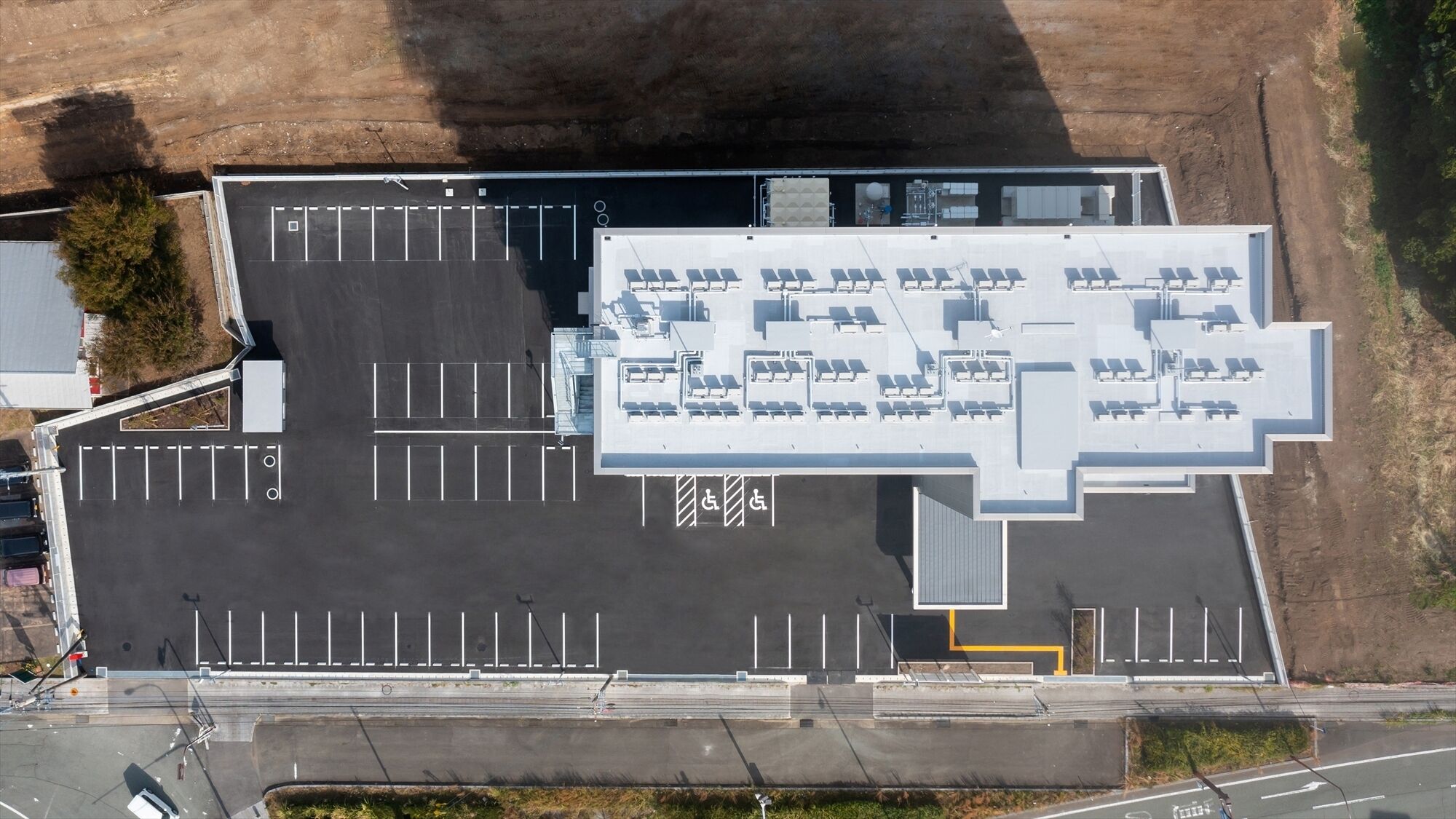 Eine Luftaufnahme eines Parkplatzes mit markierten Stellplätzen, einem überdachten Bereich mit Sitzgelegenheiten und einem Gebäude mit flachem Dach.
