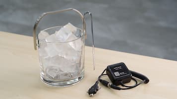 A glass container with ice and a mobile charger on a wooden surface.