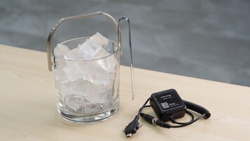 Recipiente de vidro com gelo e um carregador de celular sobre uma superfície de madeira.