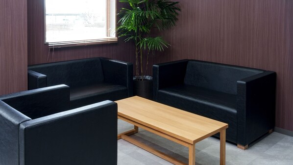 A room with a wooden table, two black sofas, and a potted plant. - Workers Hotel Kumamoto Ozu (Ozu)