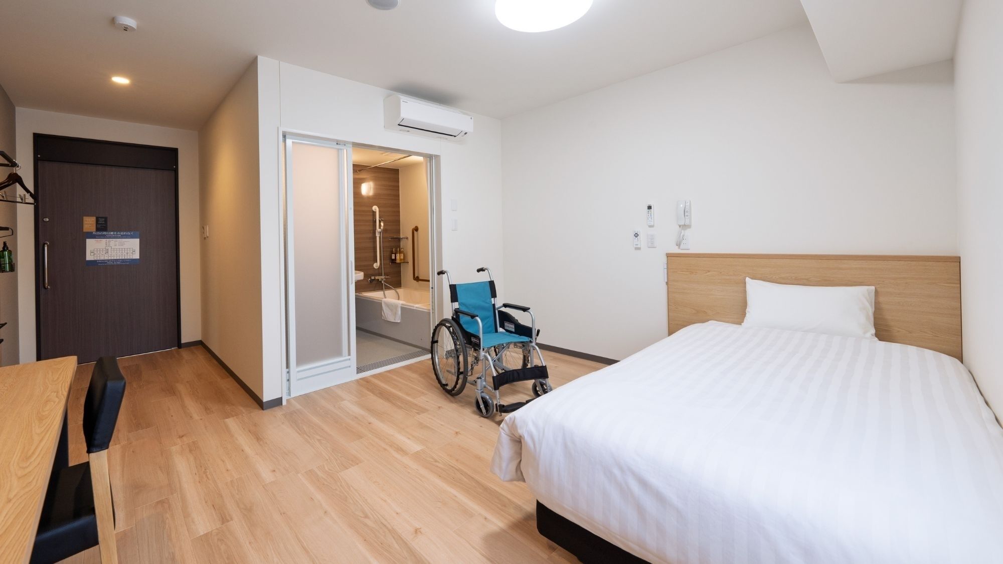 A hotel room with a bed, wheelchair, and a bathroom with a shower.