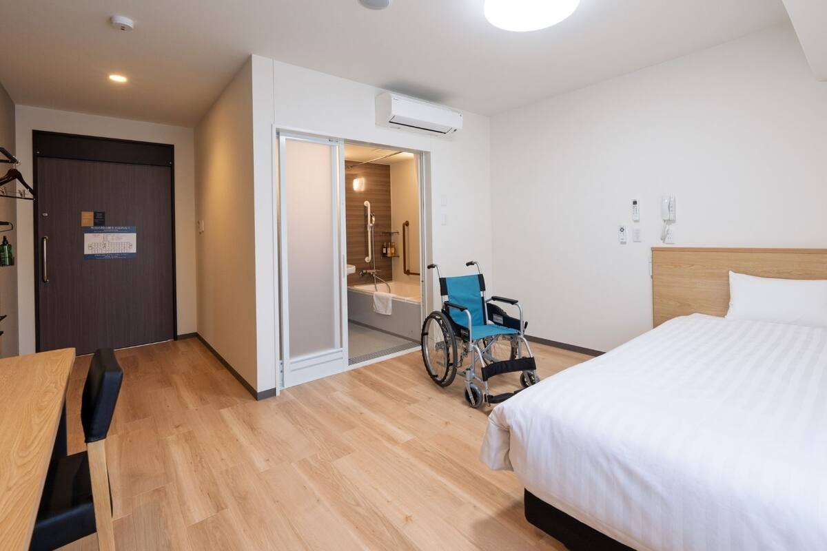 Ein Hotelzimmer mit Bett, Rollstuhl und einem Badezimmer mit Dusche.