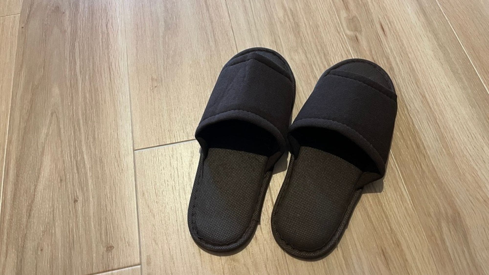 A pair of black slippers with a textured sole on a wooden floor.
