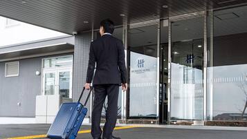 A man in a suit walking towards a hotel entrance with a blue suitcase.