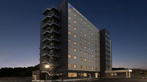 A multi-story hotel with a prominent external staircase, a flat facade with evenly spaced windows, and a clear sky at dusk. - Workers Hotel Kumamoto Ozu (Ozu)