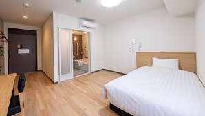 Une chambre d’hôtel comprenant un lit, un bureau, un espace douche et une porte.