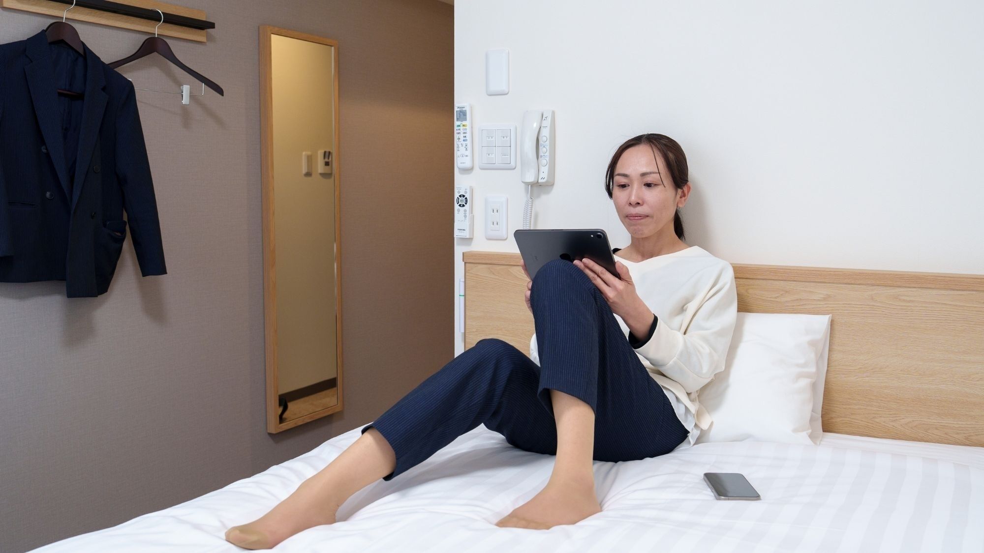 Una persona sentada en una cama en una habitación de hotel, sosteniendo una tableta.