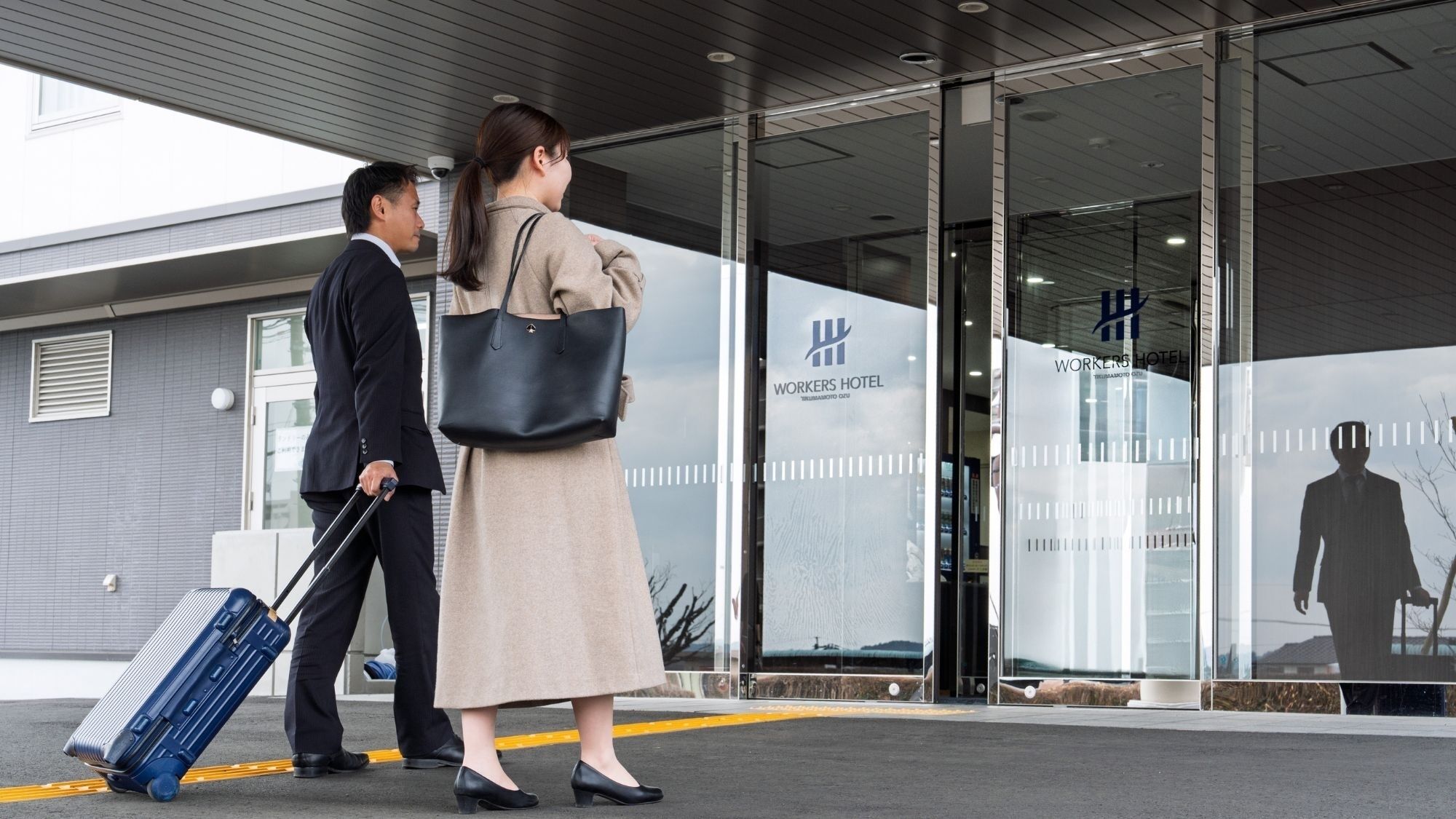 A building with a glass facade, a sign reading 'WORKERS HOTEL,' and a person with a suitcase.