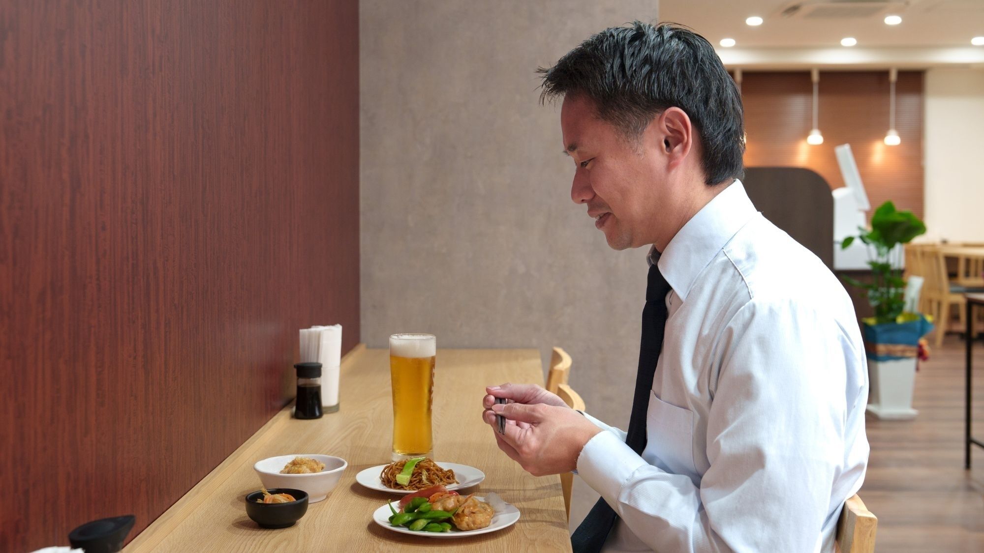Um homem jantando à mesa, com uma cerveja, pratos de comida e acompanhamentos.