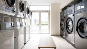 Une buanderie moderne équipée de plusieurs machines à laver et de plusieurs sèche-linge, d’un banc et offrant une vue sur l’extérieur grâce à une porte vitrée.