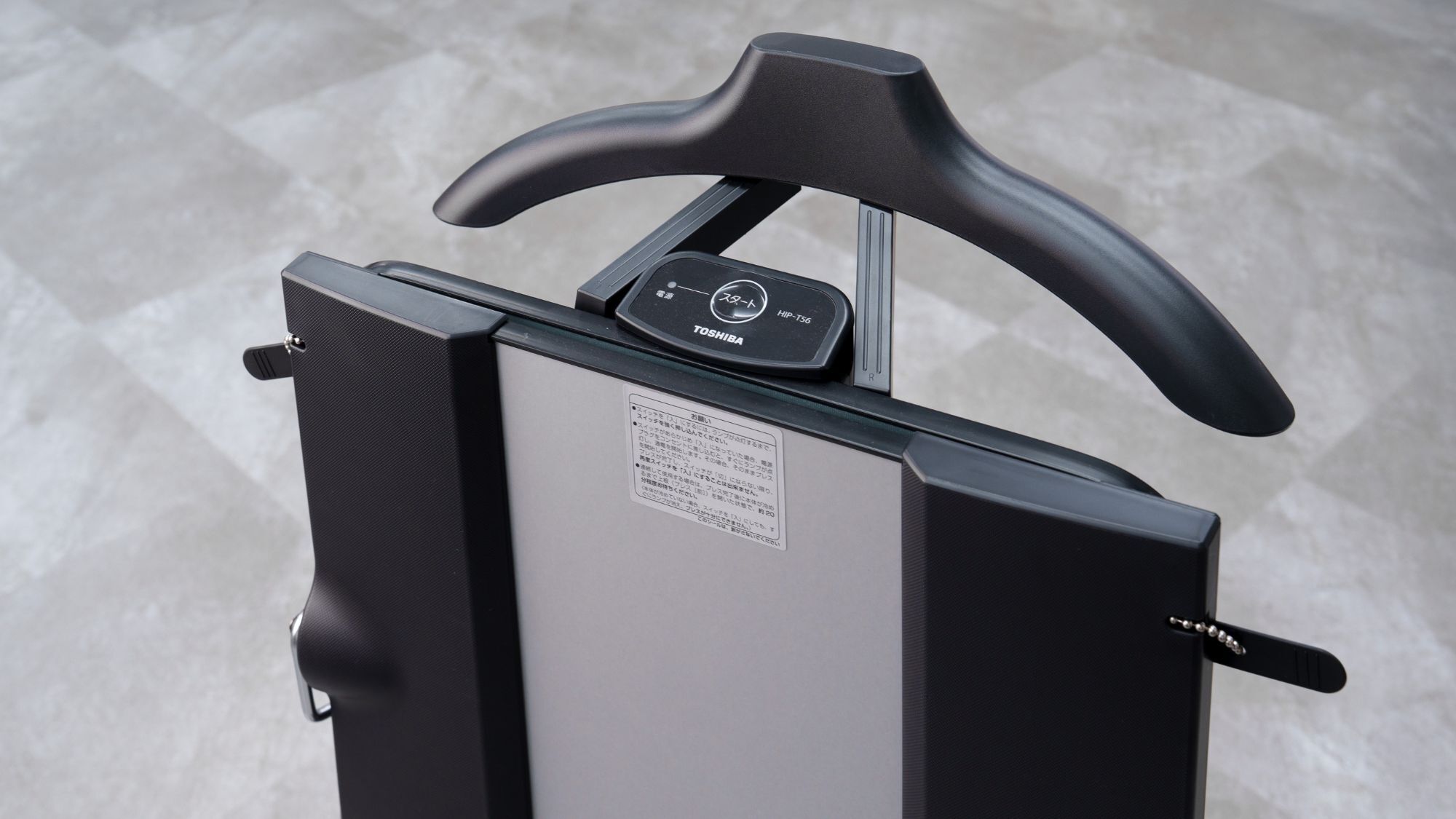 A black suitcase with a handle and wheels, featuring a label and a small control panel with a button and a display.