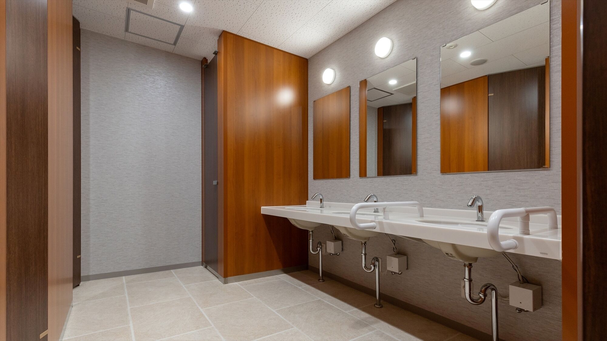 Un baño moderno con tres lavamanos, paneles de madera y un espejo grande.