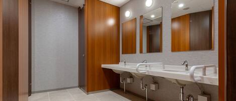Un baño moderno con tres lavamanos, paneles de madera y un espejo grande.