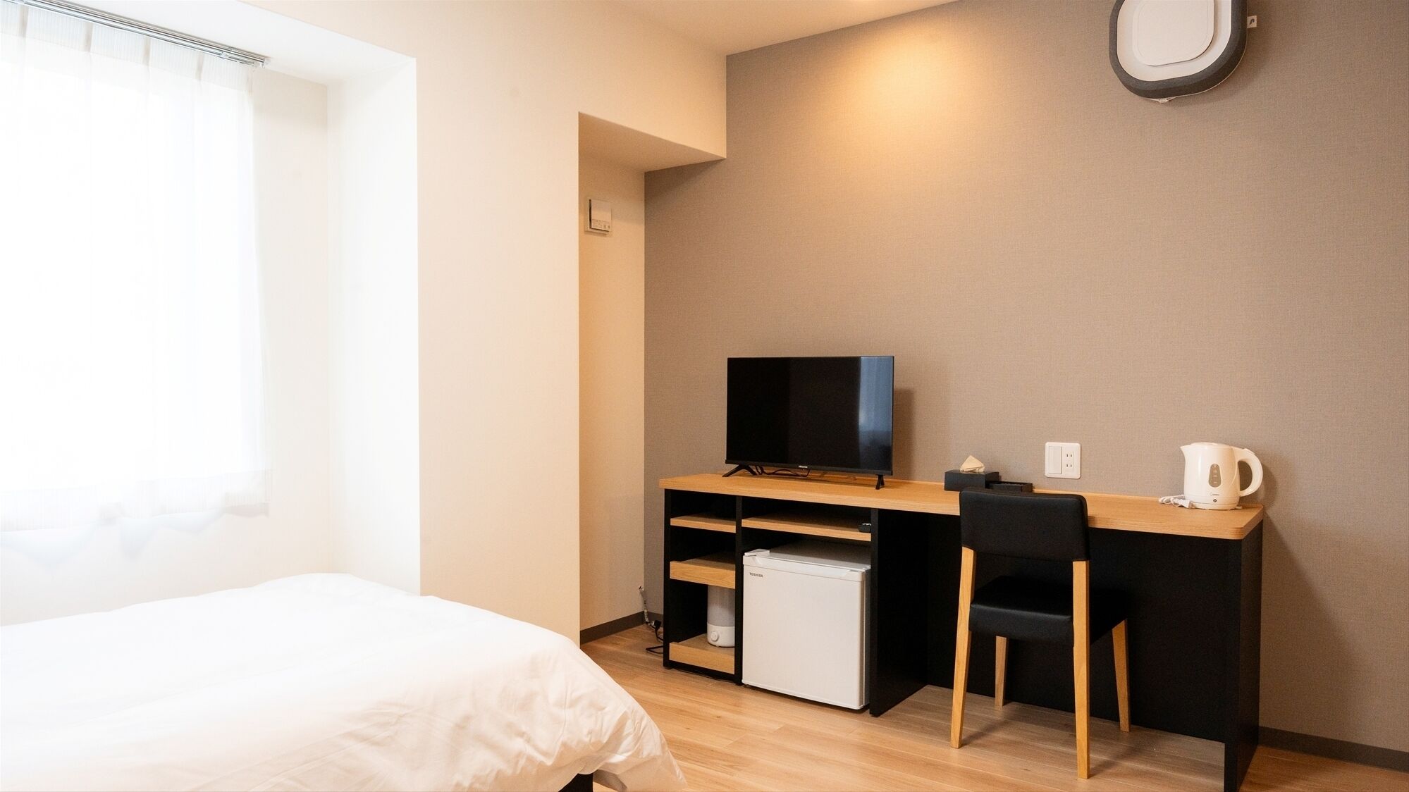Une chambre d’hôtel équipée d’un lit, d’un bureau avec une télévision, d’un petit réfrigérateur, d’une chaise et d’une bouilloire.