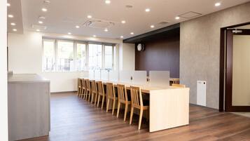 A conference room with a long table, wooden chairs, and a clock on the wall.