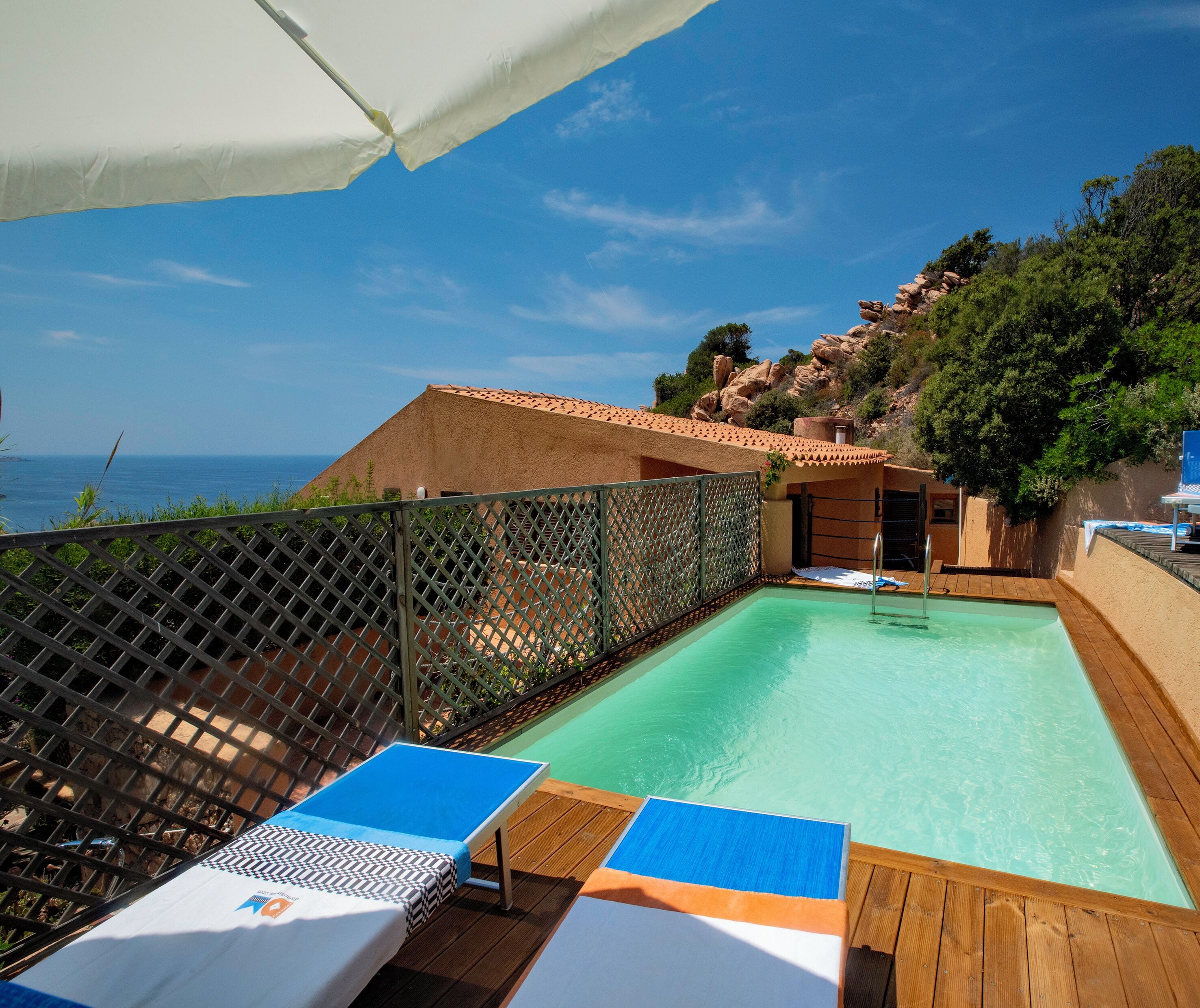Area piscina con lettini, un pontile in legno e vista sul mare.