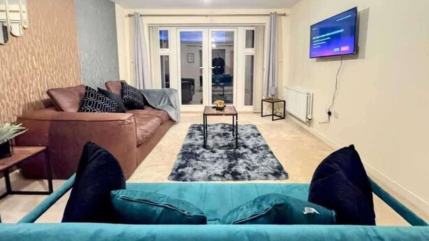 A living room with a brown sofa, a teal sofa, a coffee table, a TV mounted on the wall, and a sliding glass door leading to an outdoor area. - 3 Bedroom House Sleeps 7 - Pets Ok - Free Parking (Ashford)