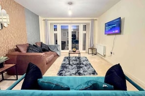 Un salon comprenant un canapé marron, un canapé turquoise, une table basse, un téléviseur fixé au mur et une porte-fenêtre coulissante donnant sur un espace extérieur.