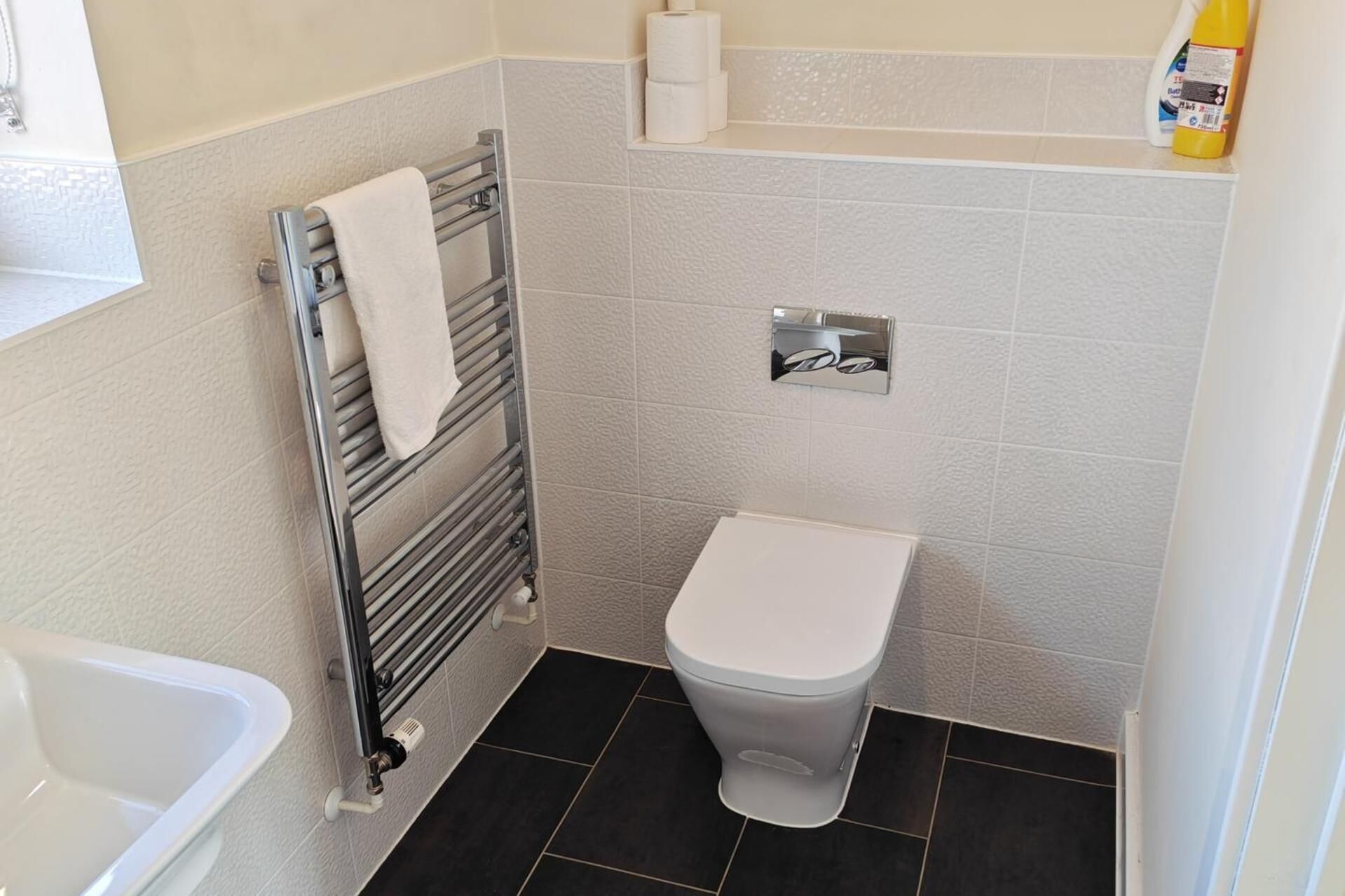 Une petite salle de bain avec des toilettes, un porte-serviettes et un flacon de produit de nettoyage accroché au mur.