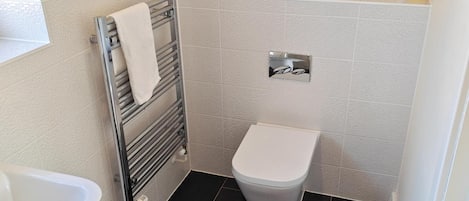 A small bathroom with a toilet, a towel rack, and a bottle of cleaning product on the wall.
