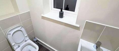 A small bathroom with a toilet, a window, and a sink.