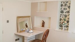 Een keurig opgeruimde slaapkamer met een bed, bureau, stoel, spiegel en raam met bloemen gordijnen.