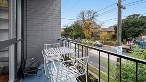 Ein Balkon mit einem Metallgeländer, einer weißen Metallbank und einem blauen Koffer auf dem Boden.