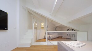 Une chambre de style loft moderne, avec un plafond en pente, un lit intégré et un escalier menant à un niveau supérieur.