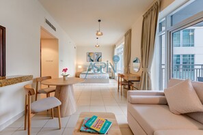 Ein modernes Wohnzimmer mit einer Couch, einem Esstisch und Stühlen. Ein großes Fenster mit Vorhängen, eine Deckenleuchte und Kunstwerke an der Wand sind ebenfalls vorhanden.