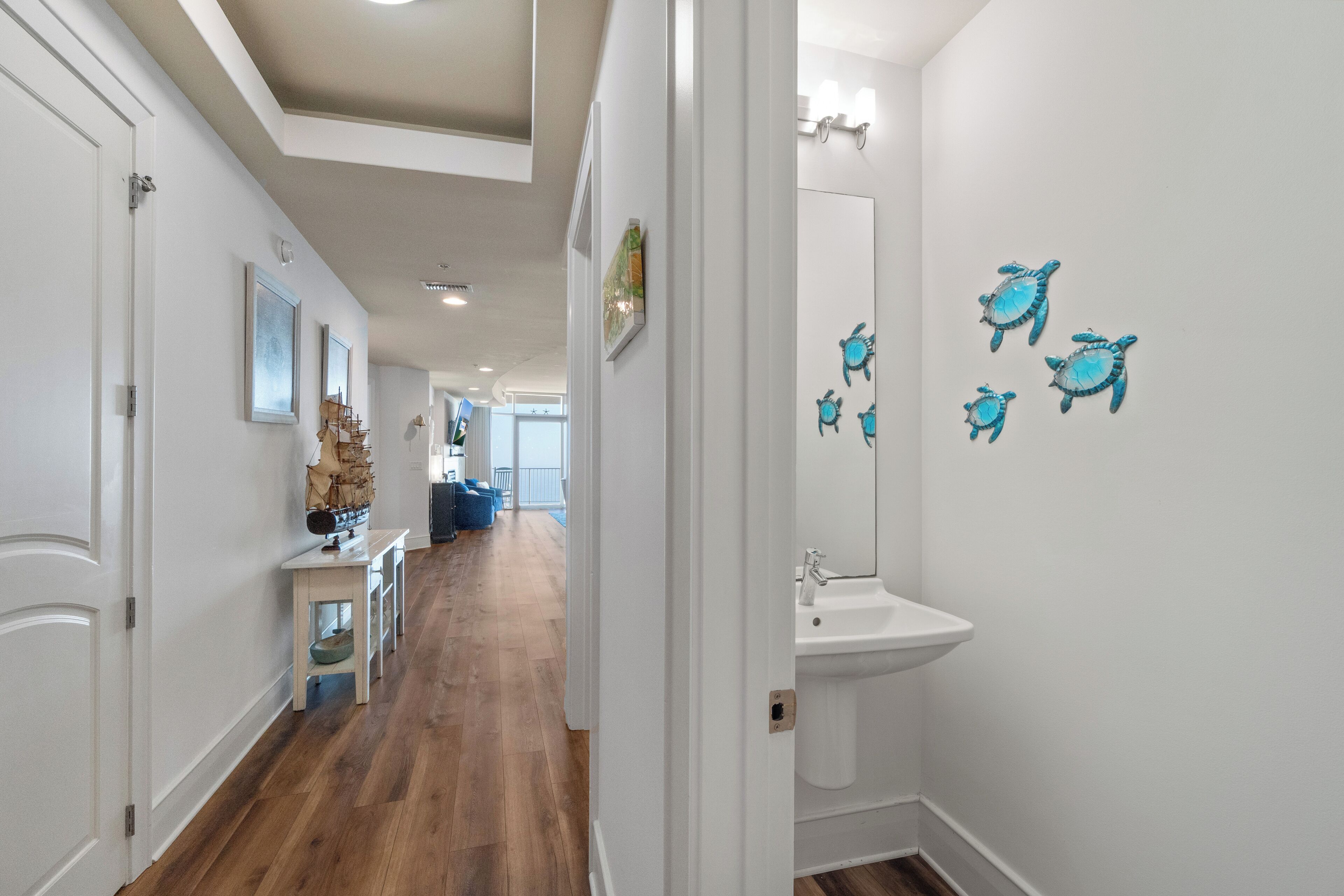 A hallway with wooden flooring, white walls, a sink, and decorative turtle wall decals.