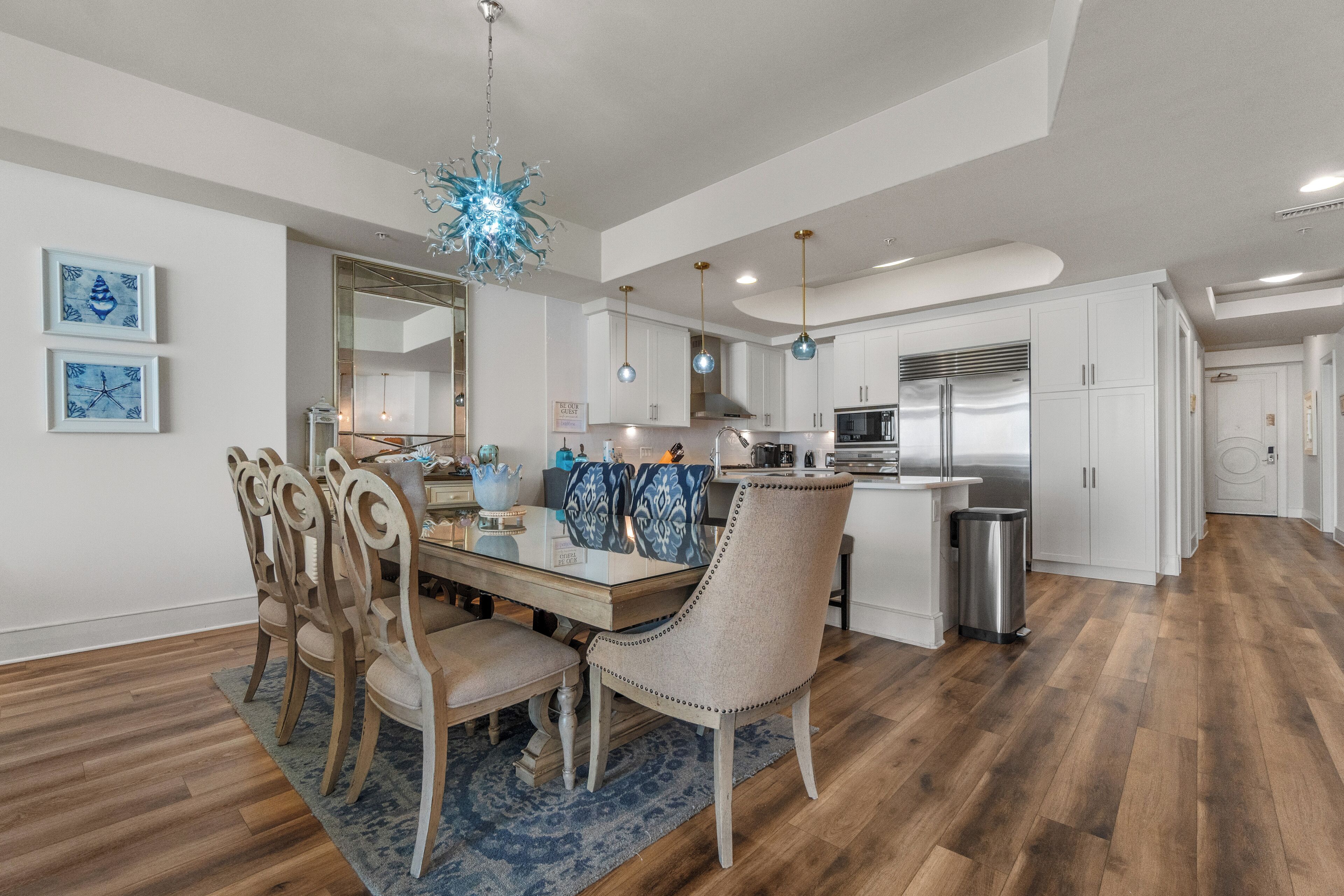 A modern kitchen with white cabinets, stainless steel appliances, and a blue chandelier.