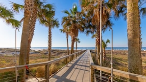 A wooden boardwalk with metal railings, surrounded by palm trees, leading to a beach with the ocean in the background. - Turquoise Place Beachside Retreat (Orange Beach)