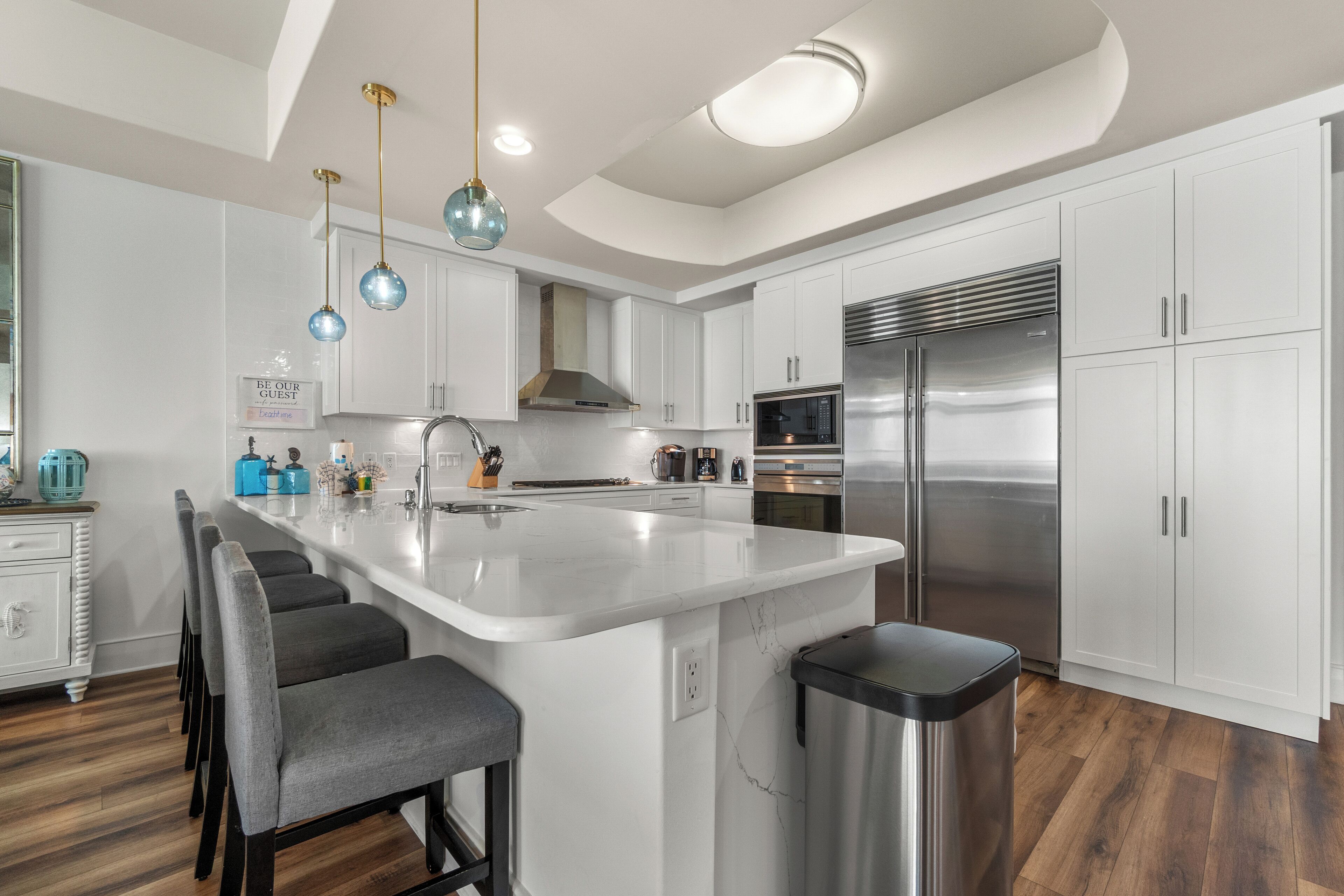 A modern kitchen with white cabinetry, a stainless steel refrigerator, and a central island with bar stools.