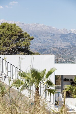 A modern building with a staircase, palm trees, and a mountainous landscape in the background. - [NEW]Villa Es-Hi w Private Pool & Scenic Sea View (Kalyves)